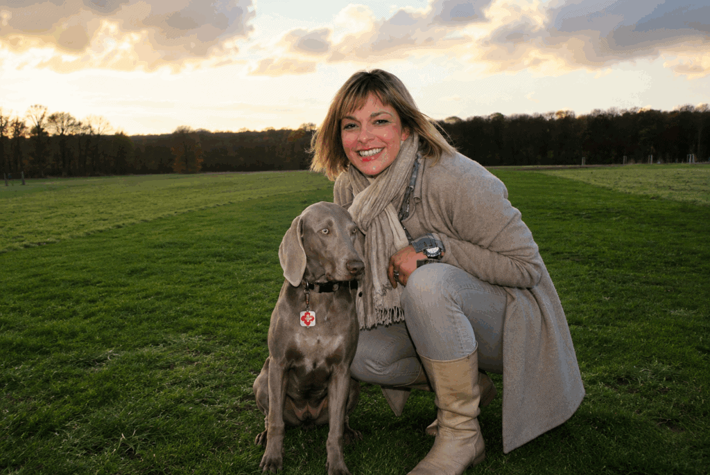 Alice Häuser kniet auf einer Wiese neben ihrer Weimaranerhündin Maya.